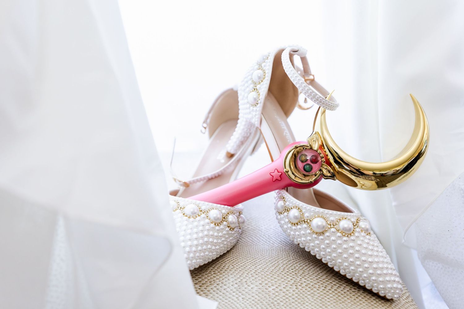 White pearl-embellished bridal shoes displayed with pink and gold magical girl wand accessory.