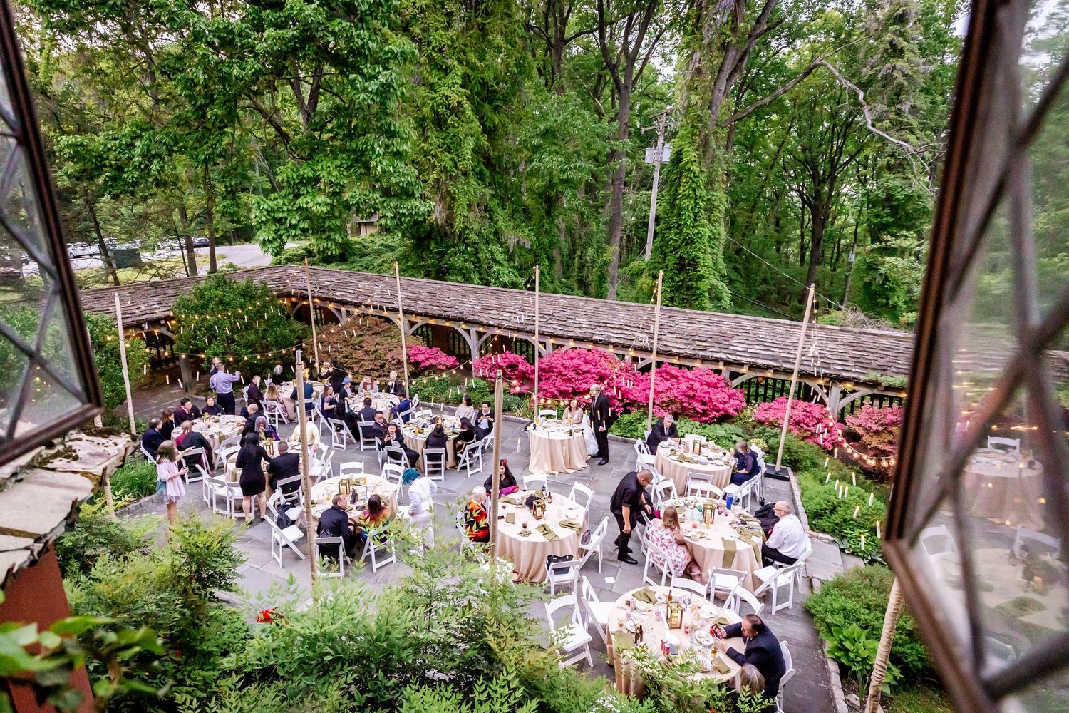 Aerial view of an outdoor wedding reception with tables and bright pink flowers.