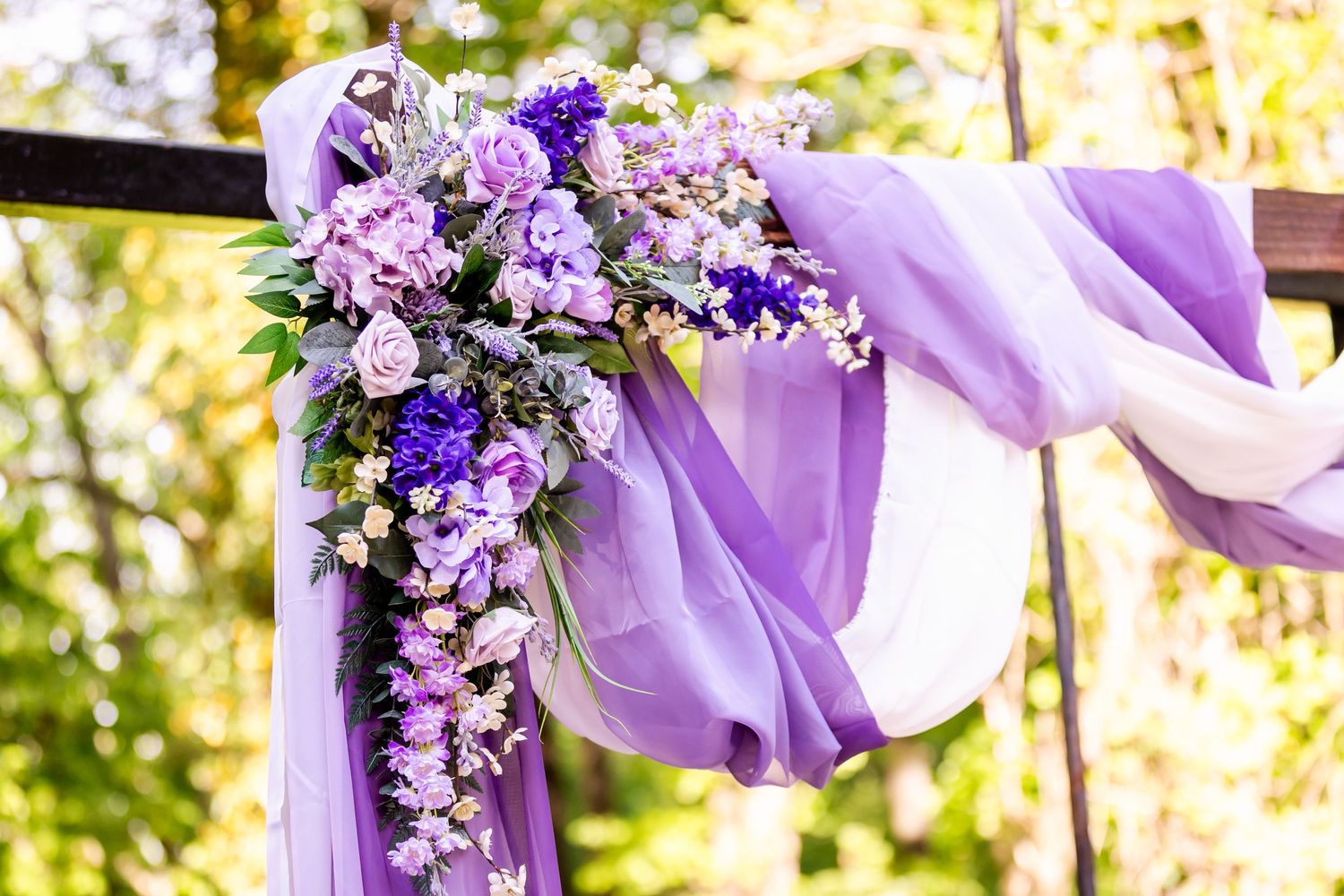 Purple and lavender floral arrangement decorating an outdoor wedding arch.