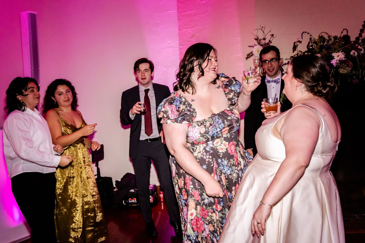 Wedding reception party with guests dancing and celebrating against pink-lit wall.