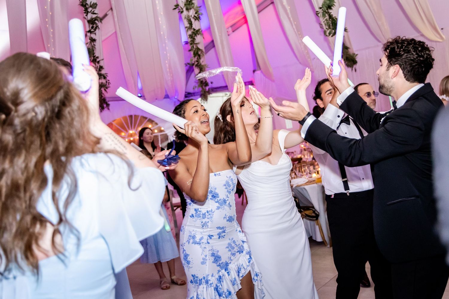 Lively wedding reception with guests dancing under pink and purple lighting.
