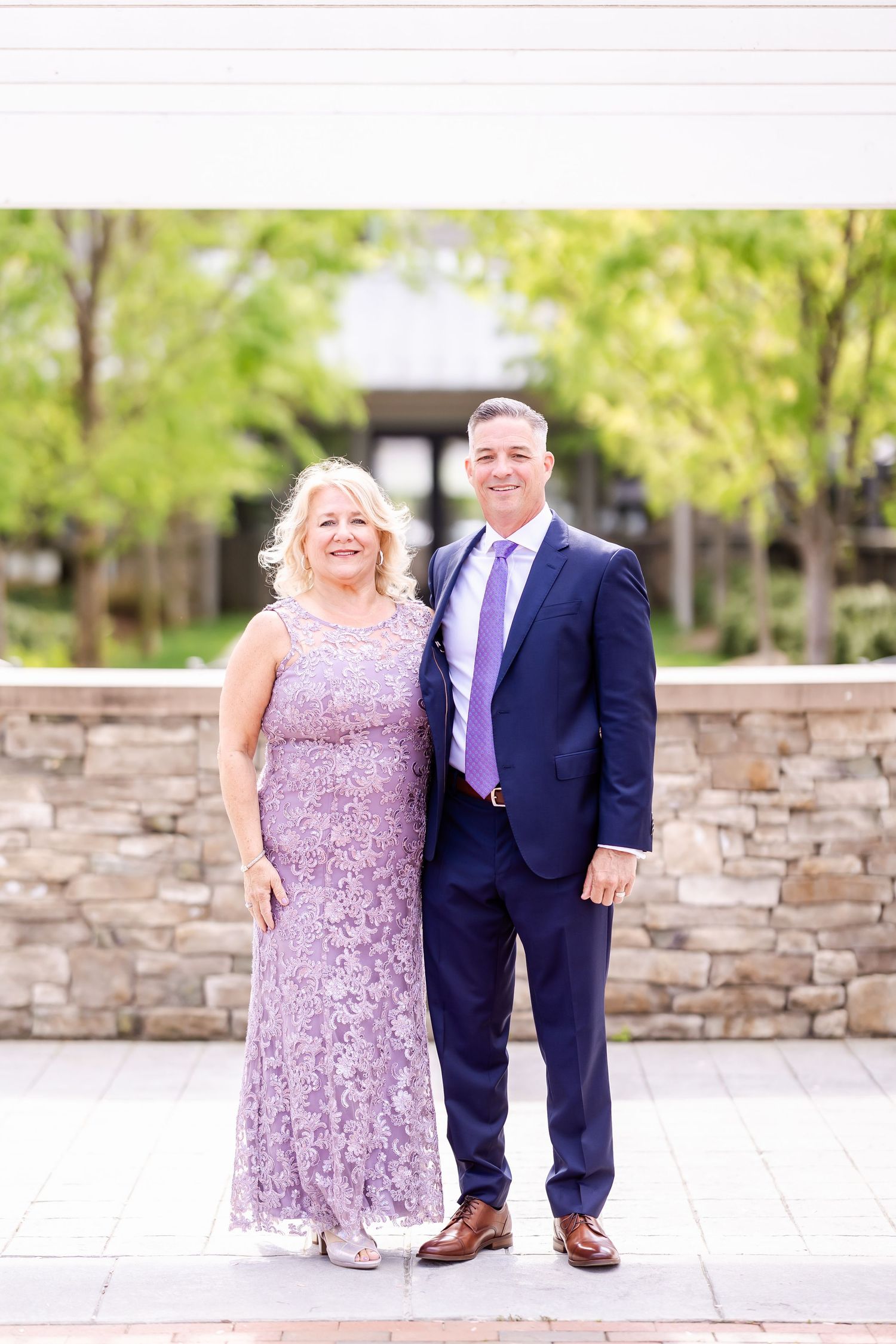 Couple poses together outdoors against stone wall backdrop during wedding celebration.