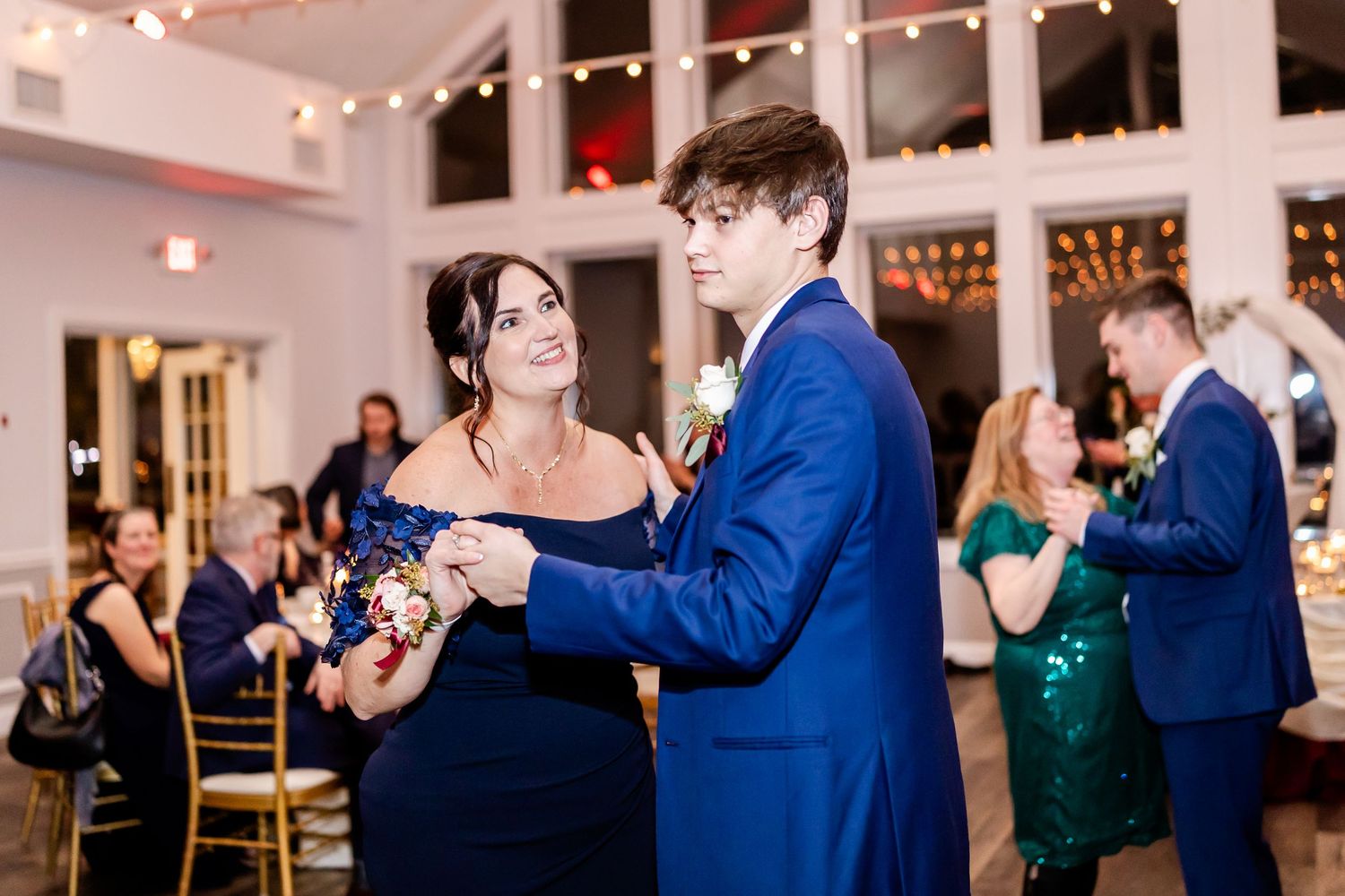 Wedding guests dancing in pairs across a wooden dance floor at an elegant indoor reception.