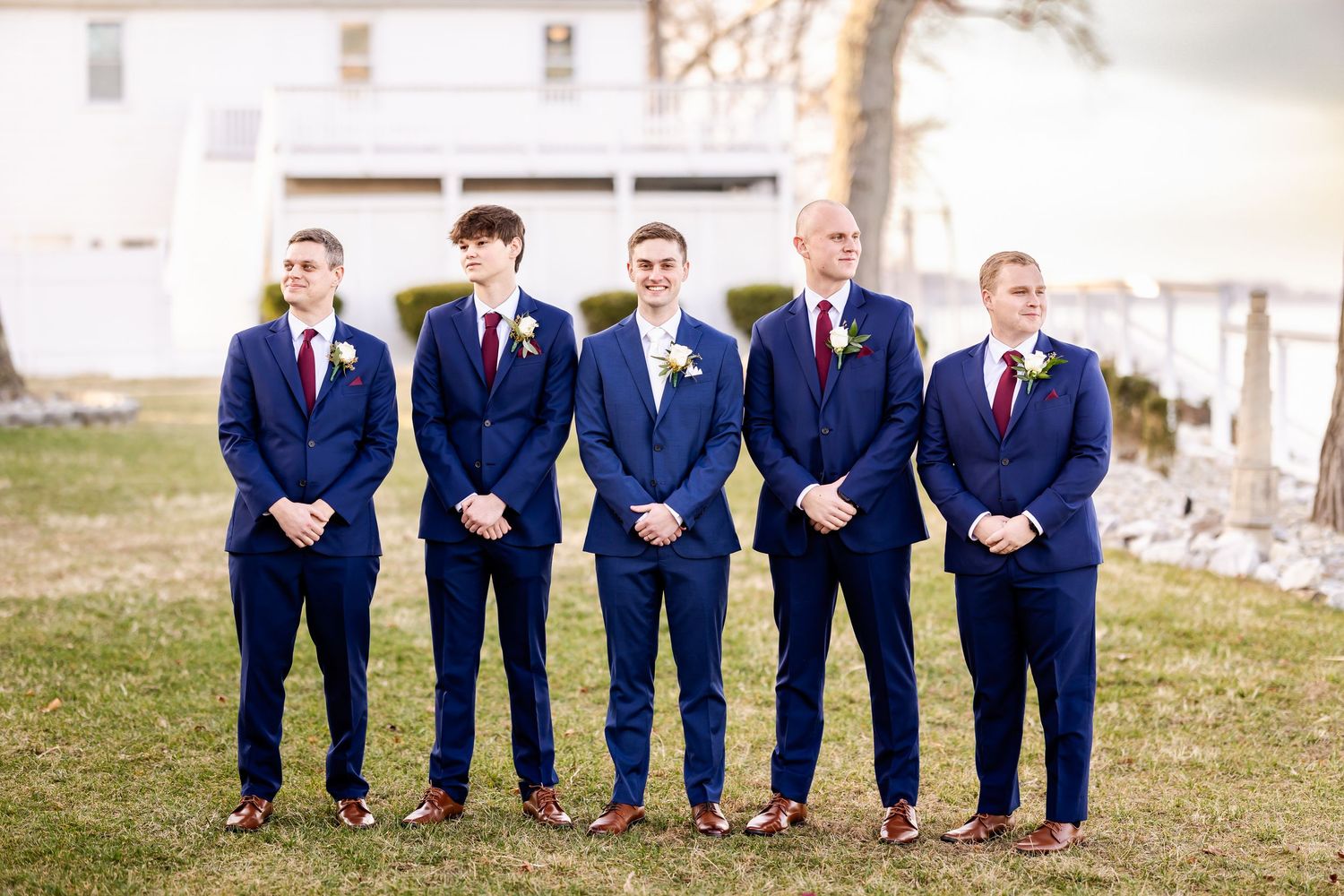 Wedding party members in navy suits sit together on a rustic wooden structure.