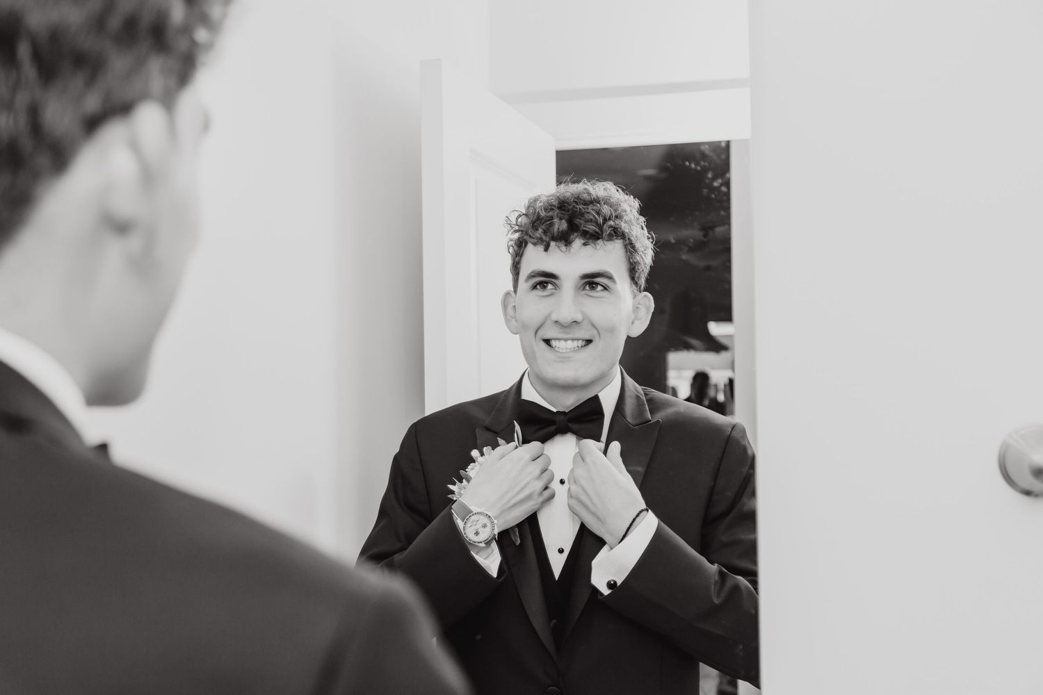 A black and white portrait of someone adjusting their bowtie while getting ready.