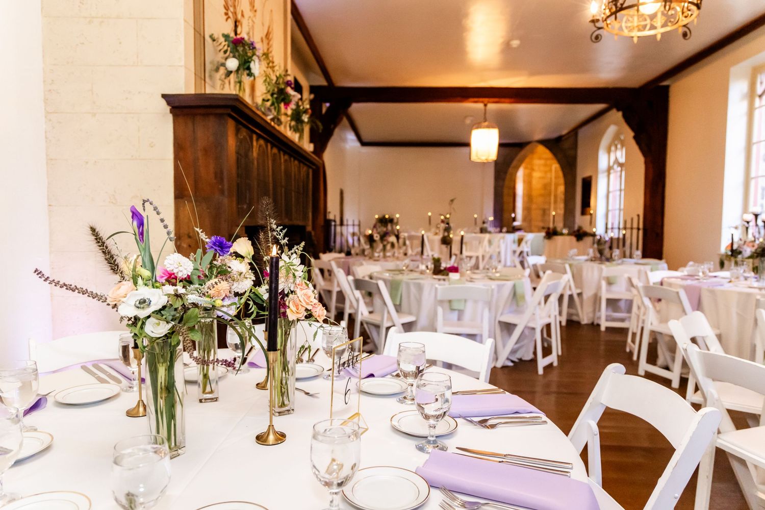 Elegant wedding reception setup with white tables, floral centerpieces, and chandeliers in a rustic wooden venue.