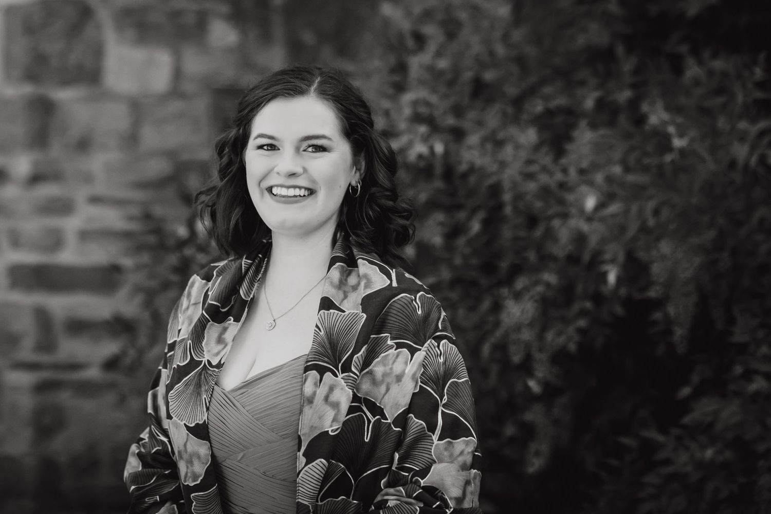 Black and white portrait of someone wearing a floral pattern jacket against a brick wall.