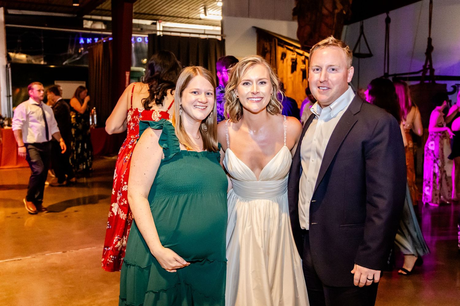 Wedding reception guests pose together in formal attire under warm lighting.