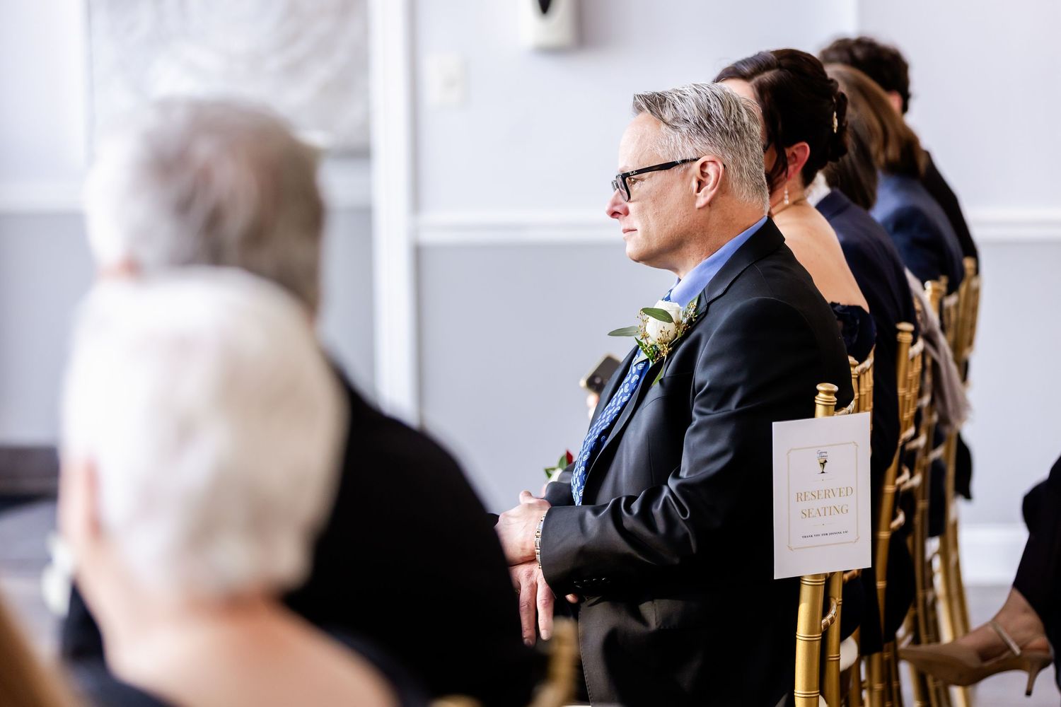 Wedding guests seated in formal attire watching ceremony proceedings.