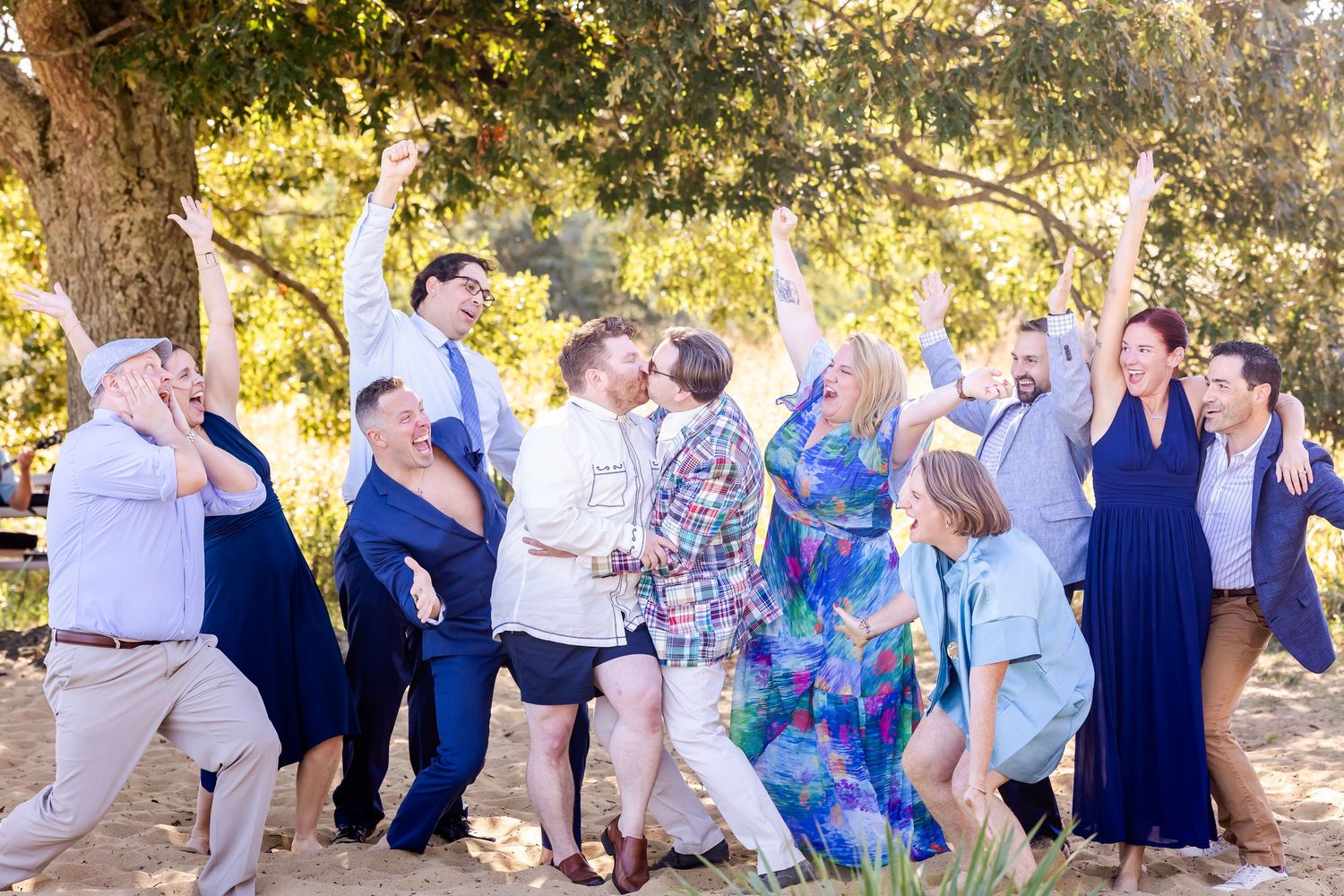 Group of wedding guests dancing together outdoors under trees at a celebration event.