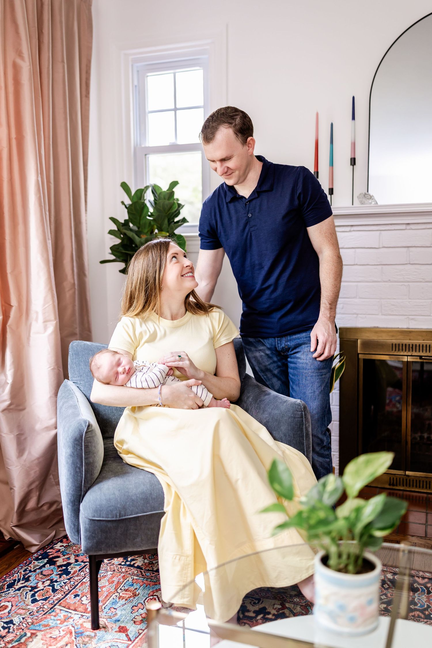 Living room scene with yellow dress and navy shirt against peach curtains and houseplants.