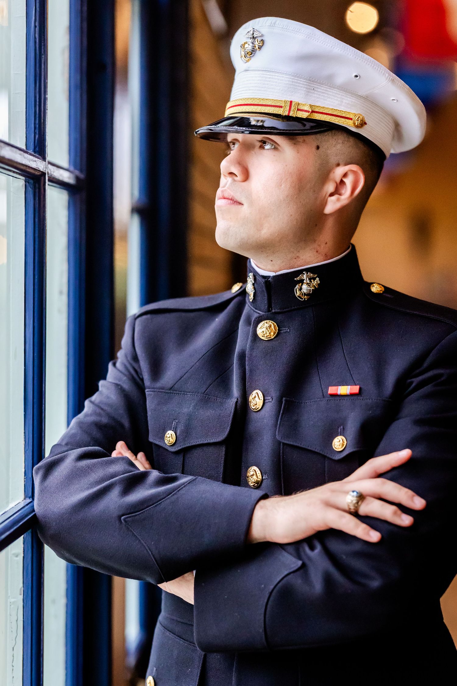 Naval officer in dress uniform leans against blue window frames in formal portrait.