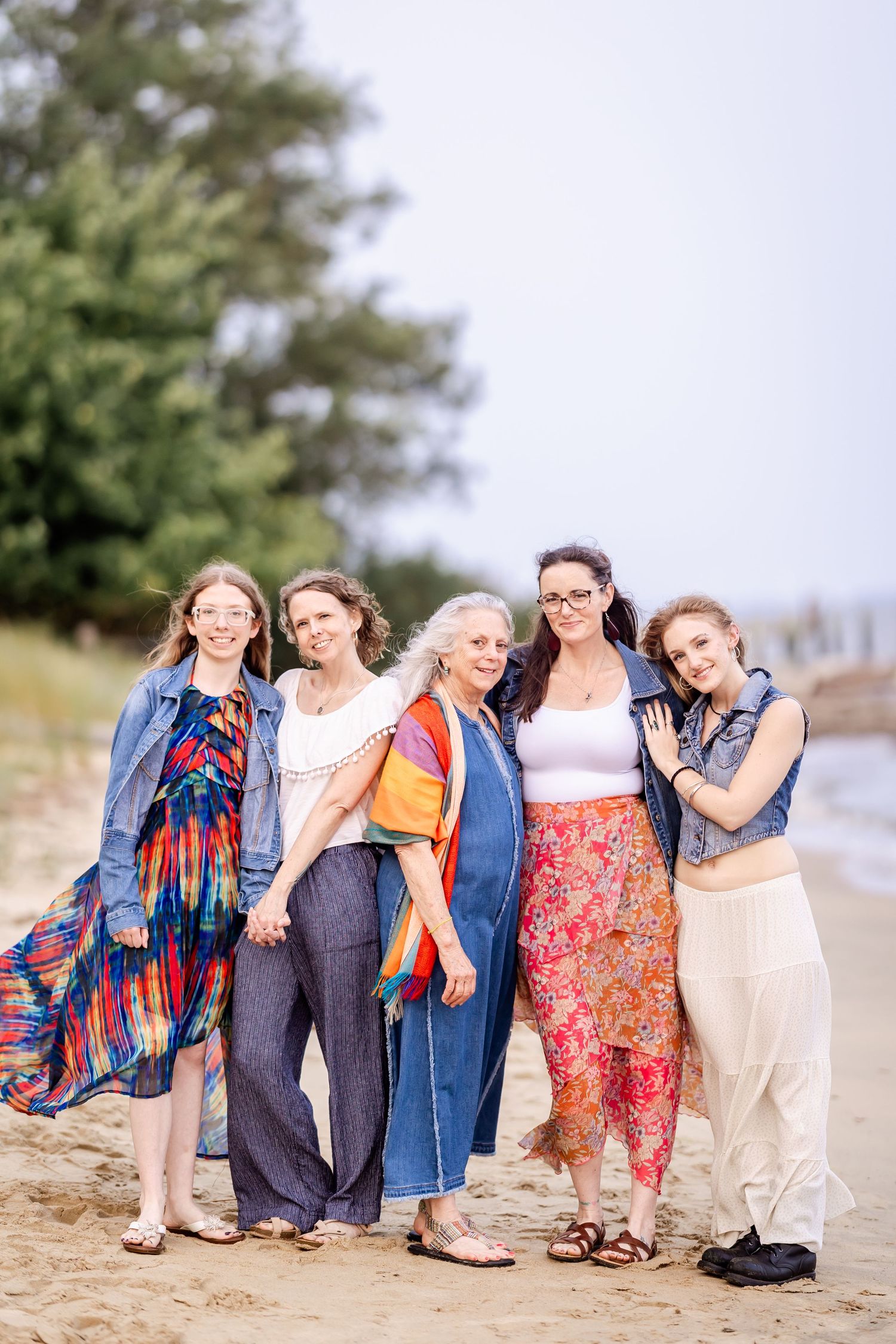 Group in denim and colorful outfits posing together on beach.