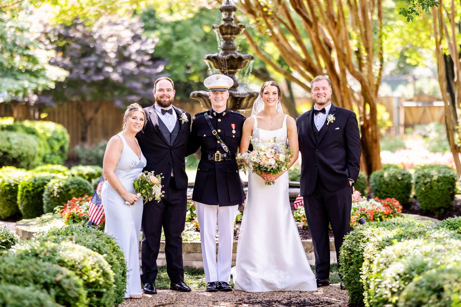Wedding party poses in formal garden setting with traditional military attire.