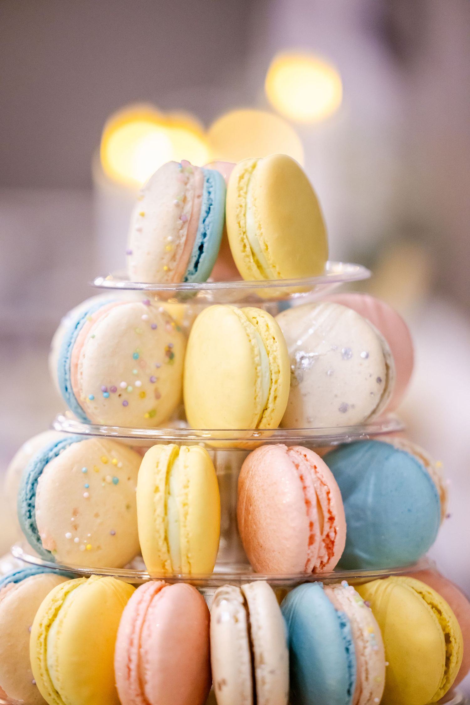 Colorful French macarons arranged in tiers on a display stand with pastel yellow, blue, pink and white cookies.