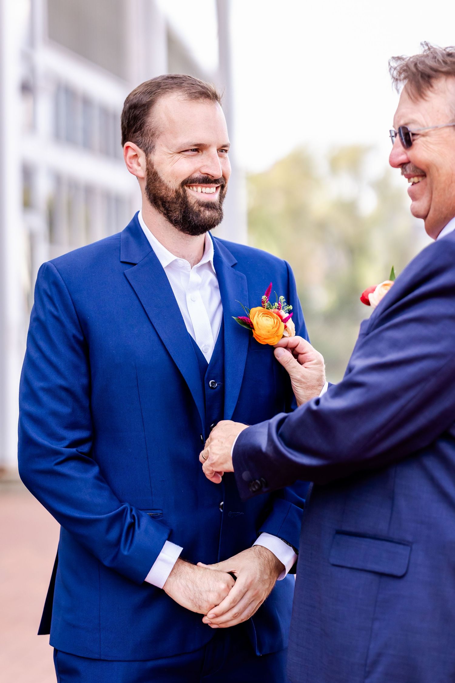 Two men in blue suits sharing a joyful moment with an orange boutonniere.
