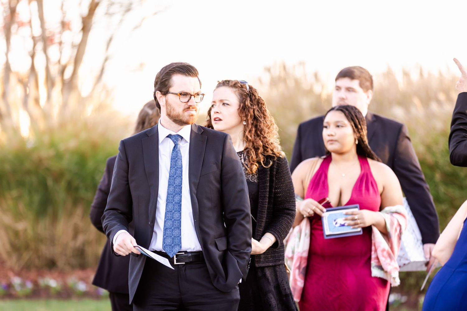 Wedding guests in formal attire socialize during an outdoor garden reception.