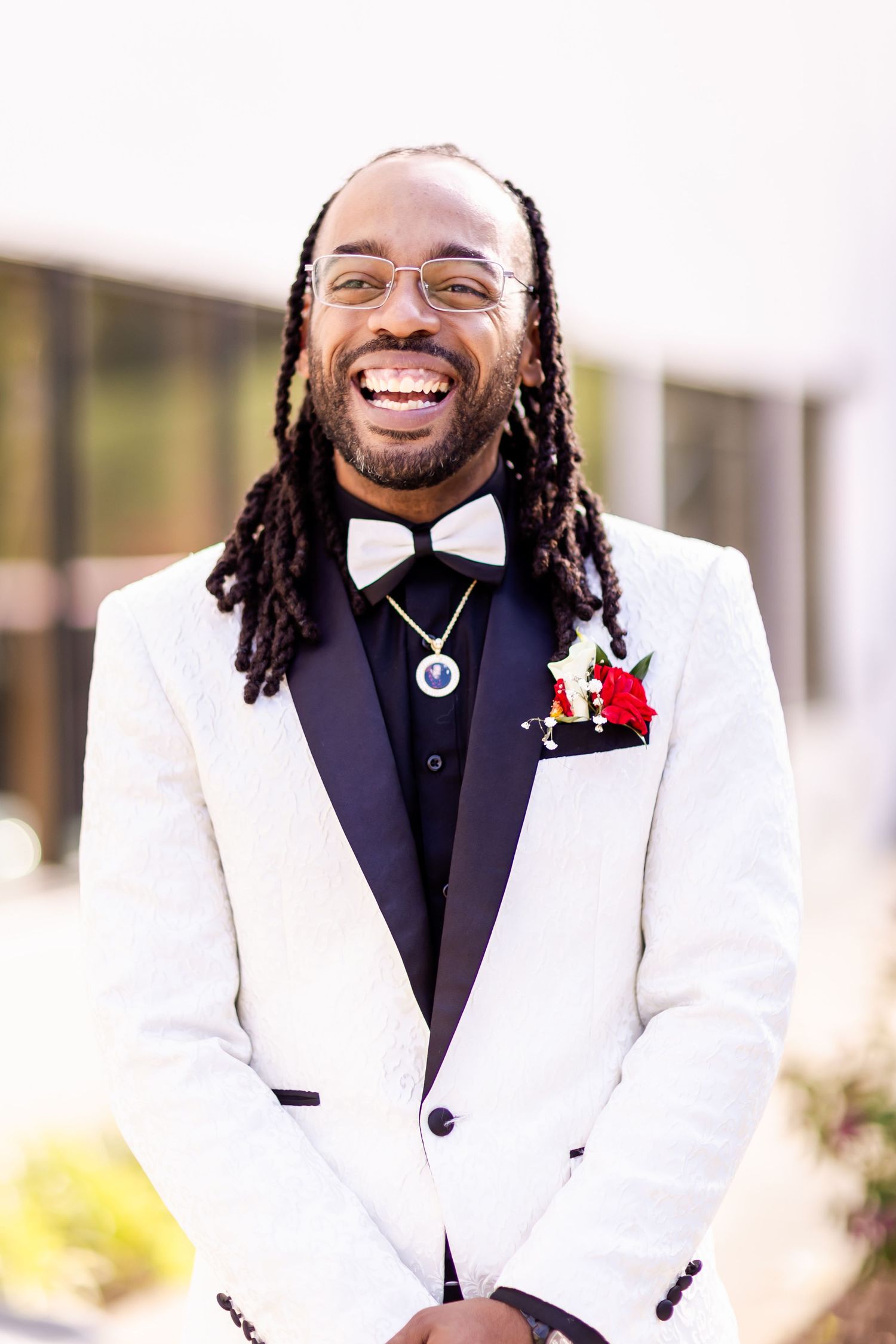 A groom in a white tuxedo jacket and bow tie smiling brightly at the camera.