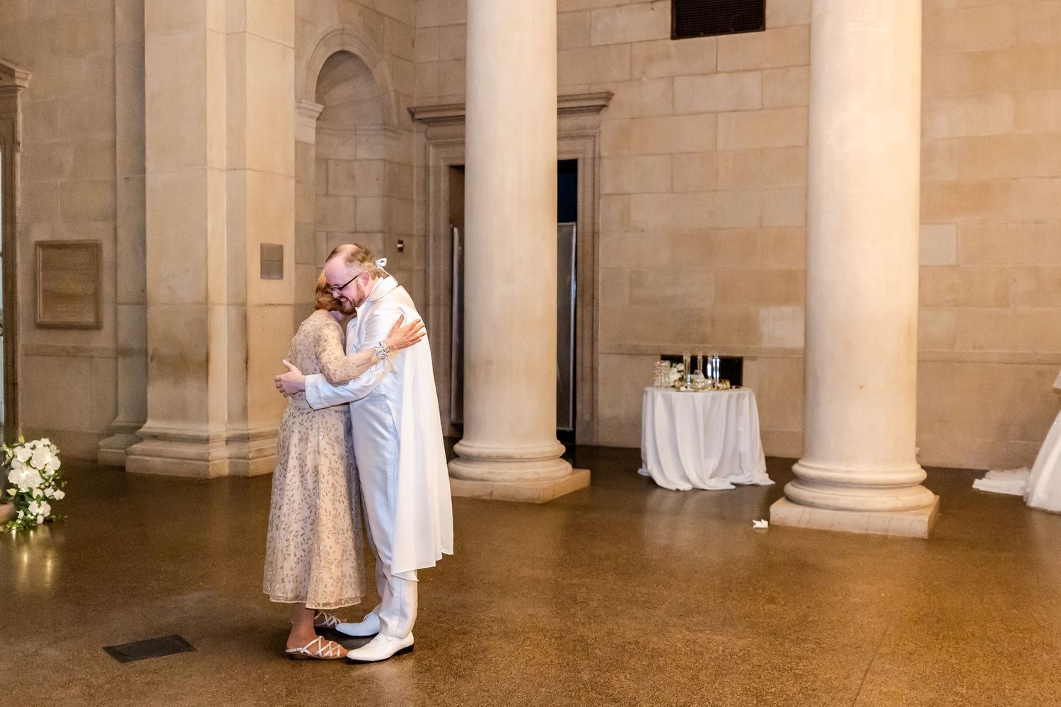 A couple embraces while dancing in an elegant hall with stone pillars and romantic lighting.