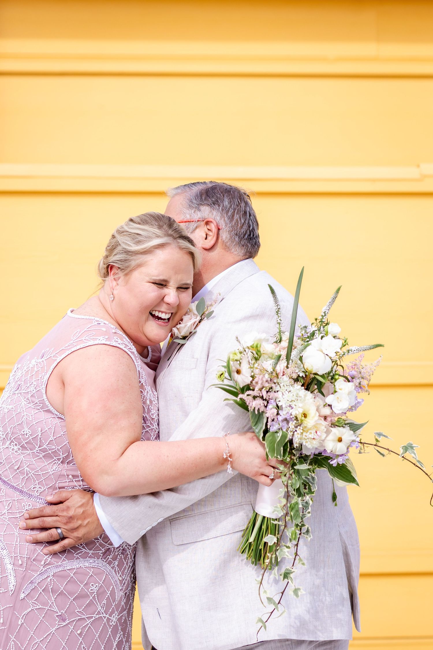 An intimate moment shared between a couple against a yellow wall with a beautiful floral bouquet.