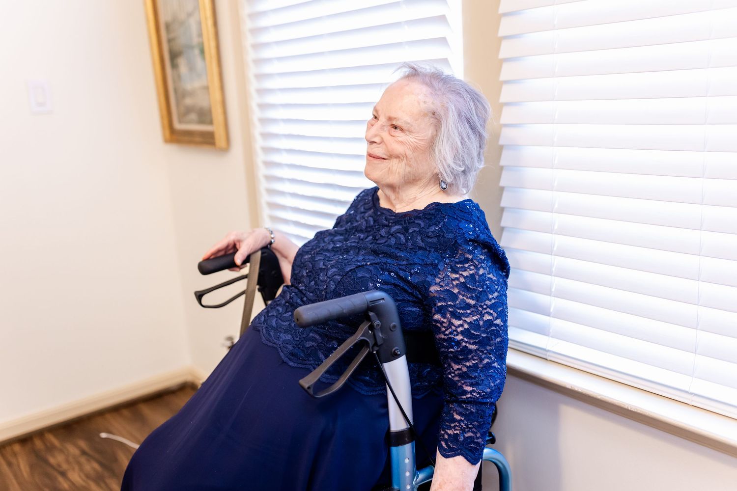 Woman in navy blue lace dress sits elegantly by window during wedding preparations.