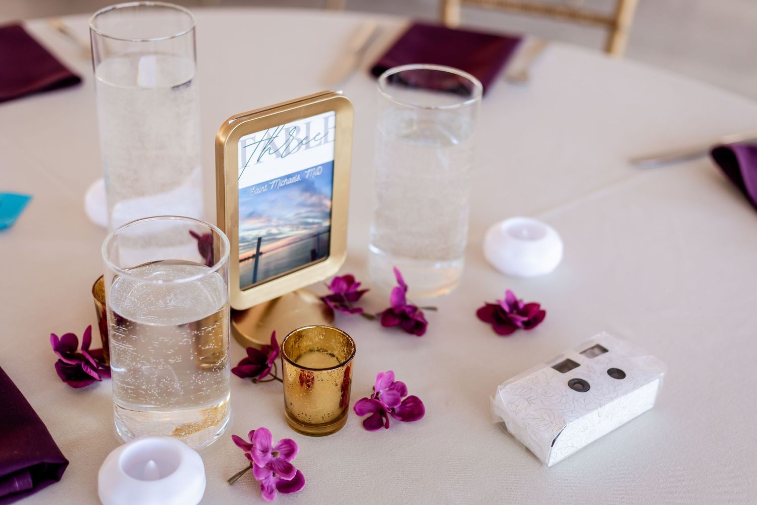 Wedding reception table setting with purple orchids, gold accents, and table number display.
