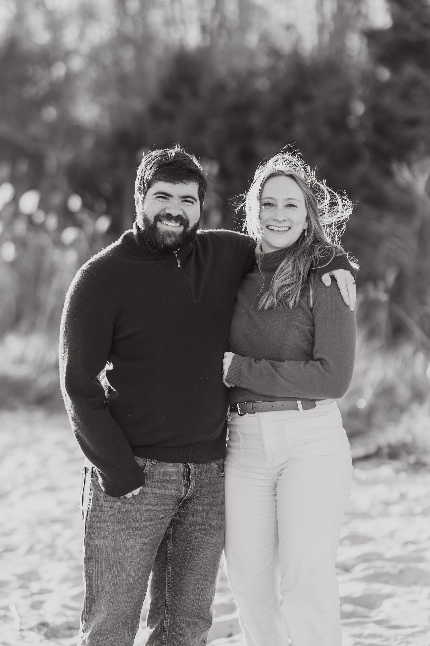 Black and white portrait of couple in casual attire standing together on beach.