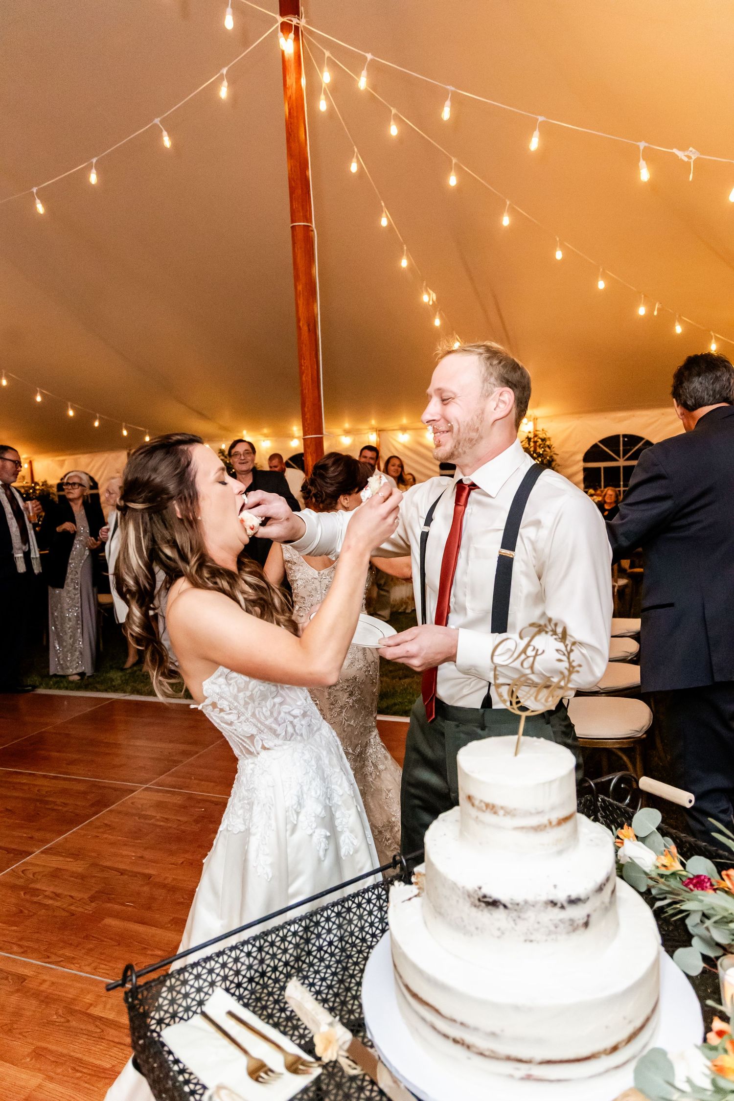 Newlyweds playfully cut their white wedding cake at the reception under string lights.