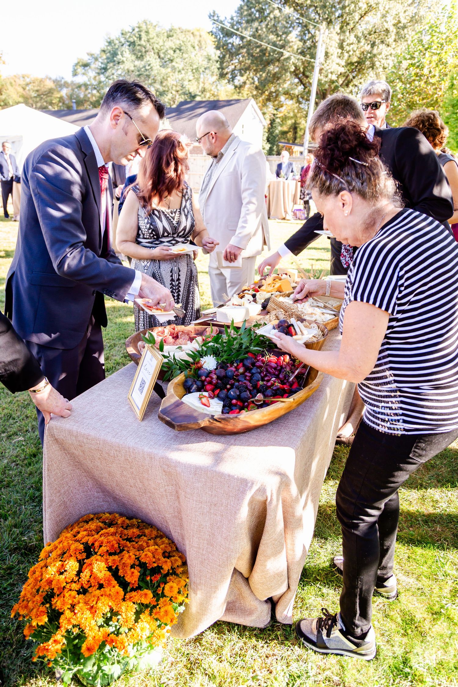 People serving themselves food at an outdoor buffet table with bright orange flowers as decoration.