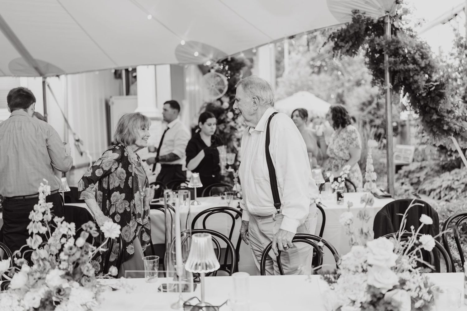 Black and white photo of wedding guests enjoying an outdoor reception under string lights.