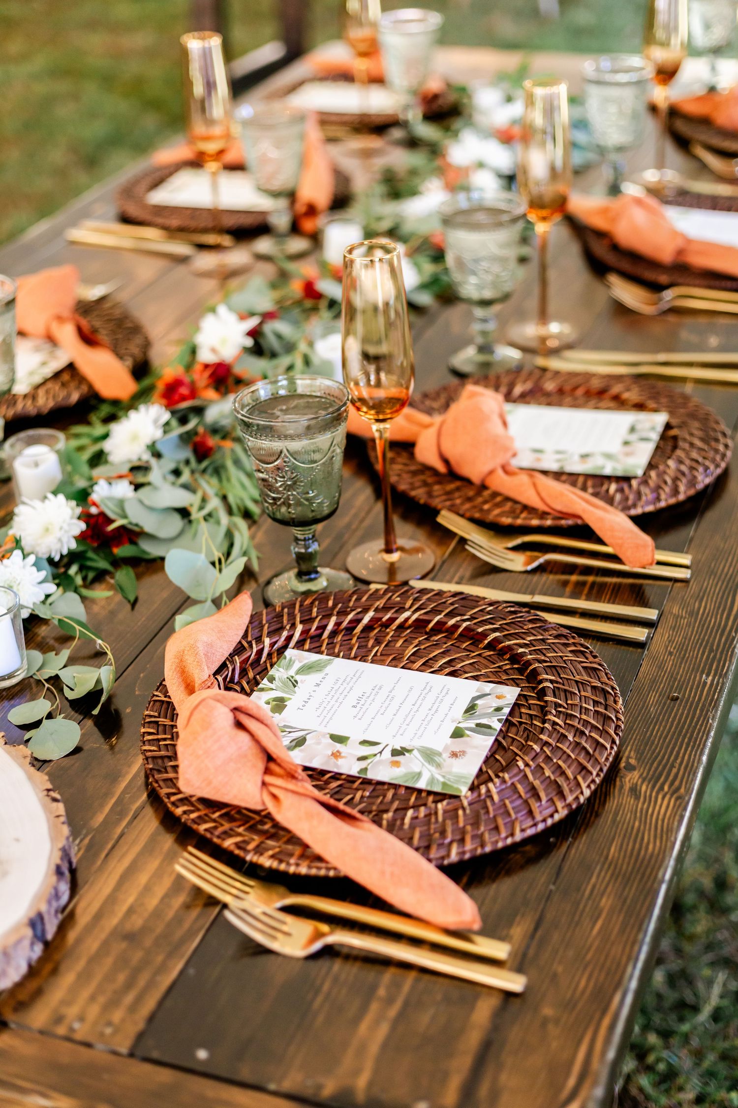 Elegant fall wedding table settings with woven chargers, peach napkins, and eucalyptus garland.