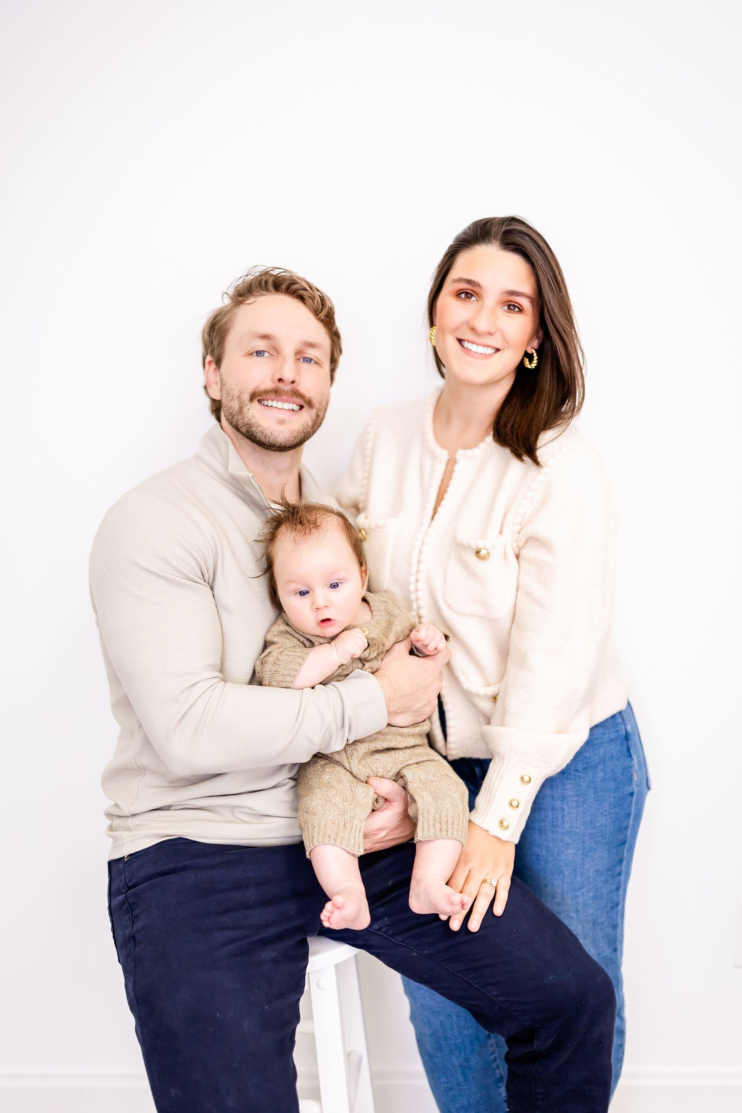 A happy family portrait with a couple and their baby posing together against a white background.