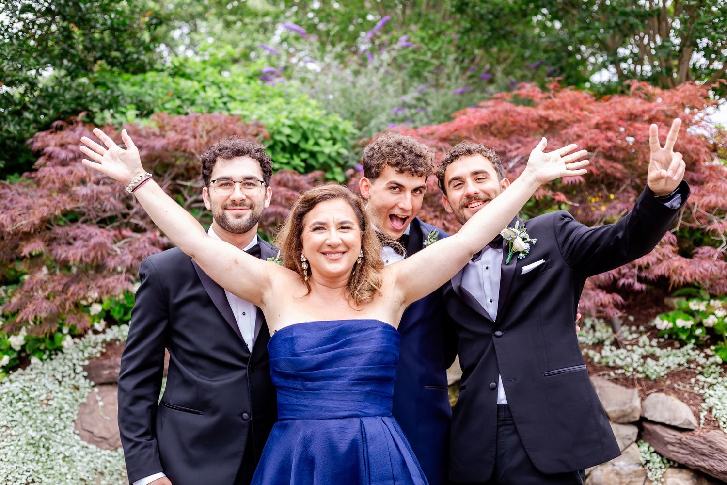 Wedding party celebrating with energetic poses in a garden setting.