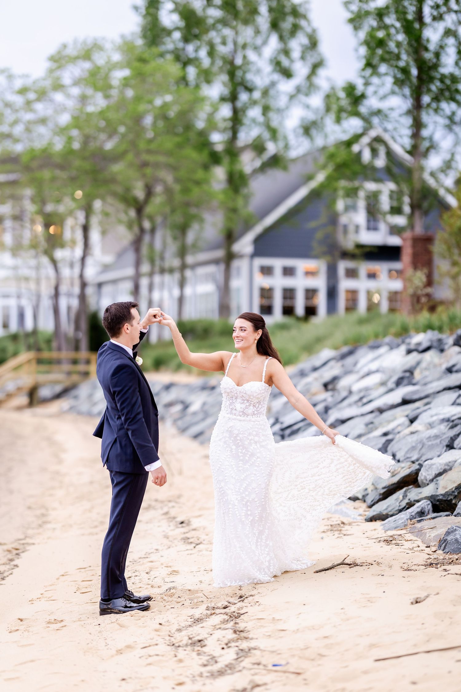 A couple dances playfully on a beach with a blue house in the background.