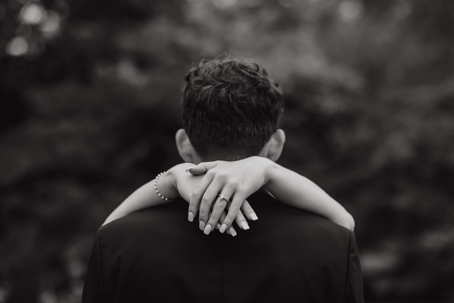 Black and white photo of a couple embracing during their wedding dance outdoors.