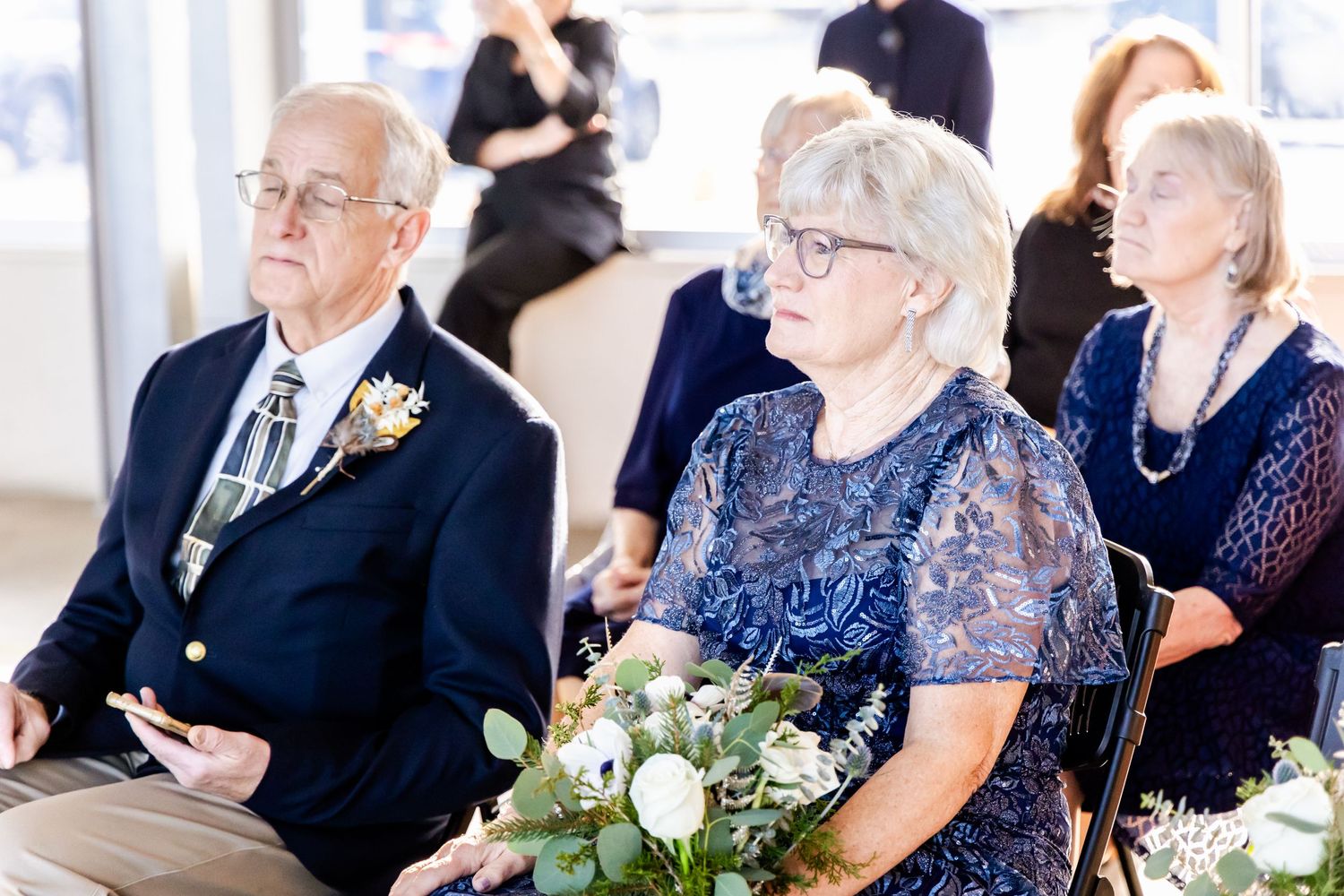 Wedding guests seated in formal attire with elegant floral bouquet on display.