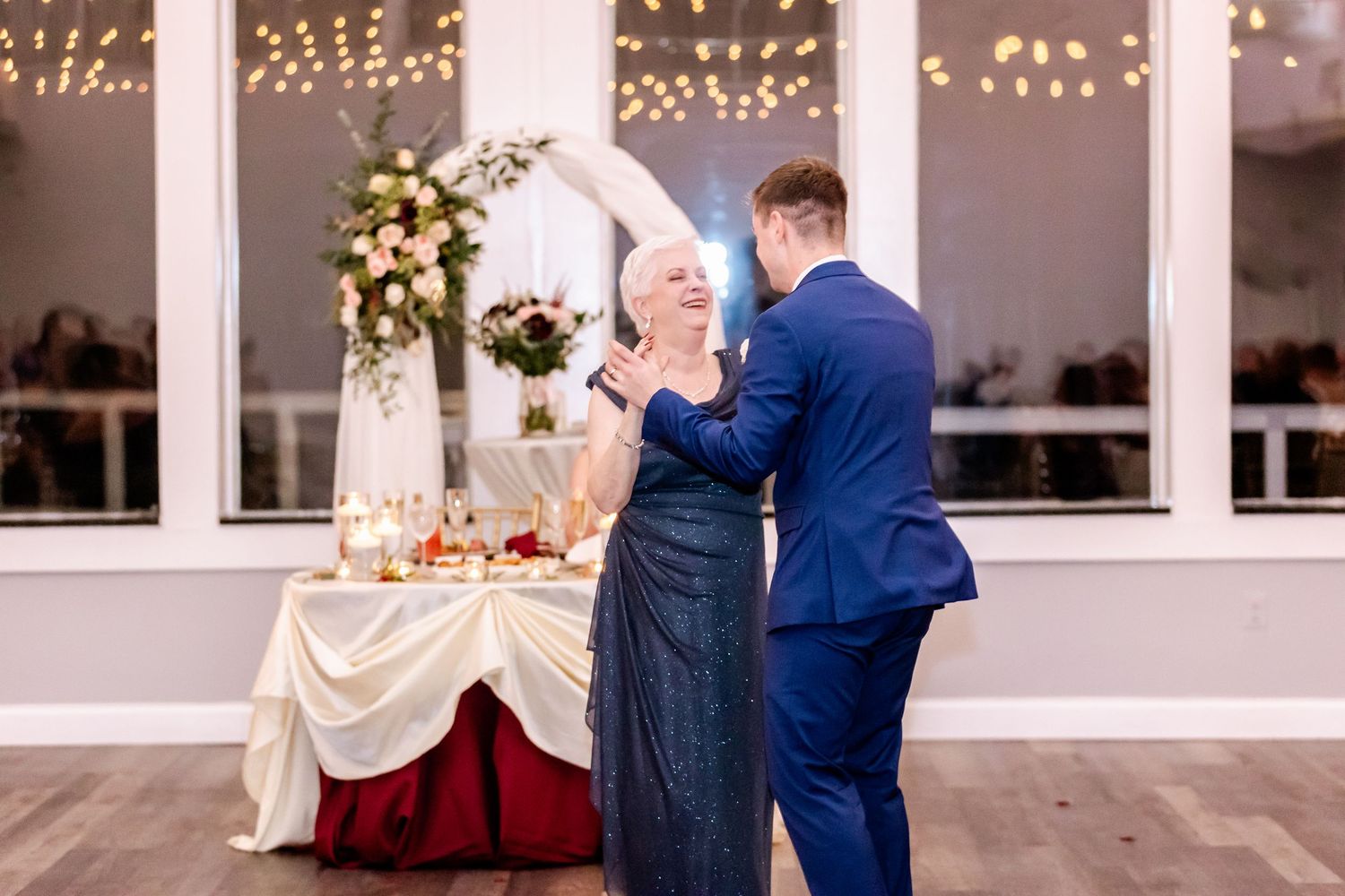 Wedding guests dancing and celebrating on a dance floor under string lights in an elegant venue.