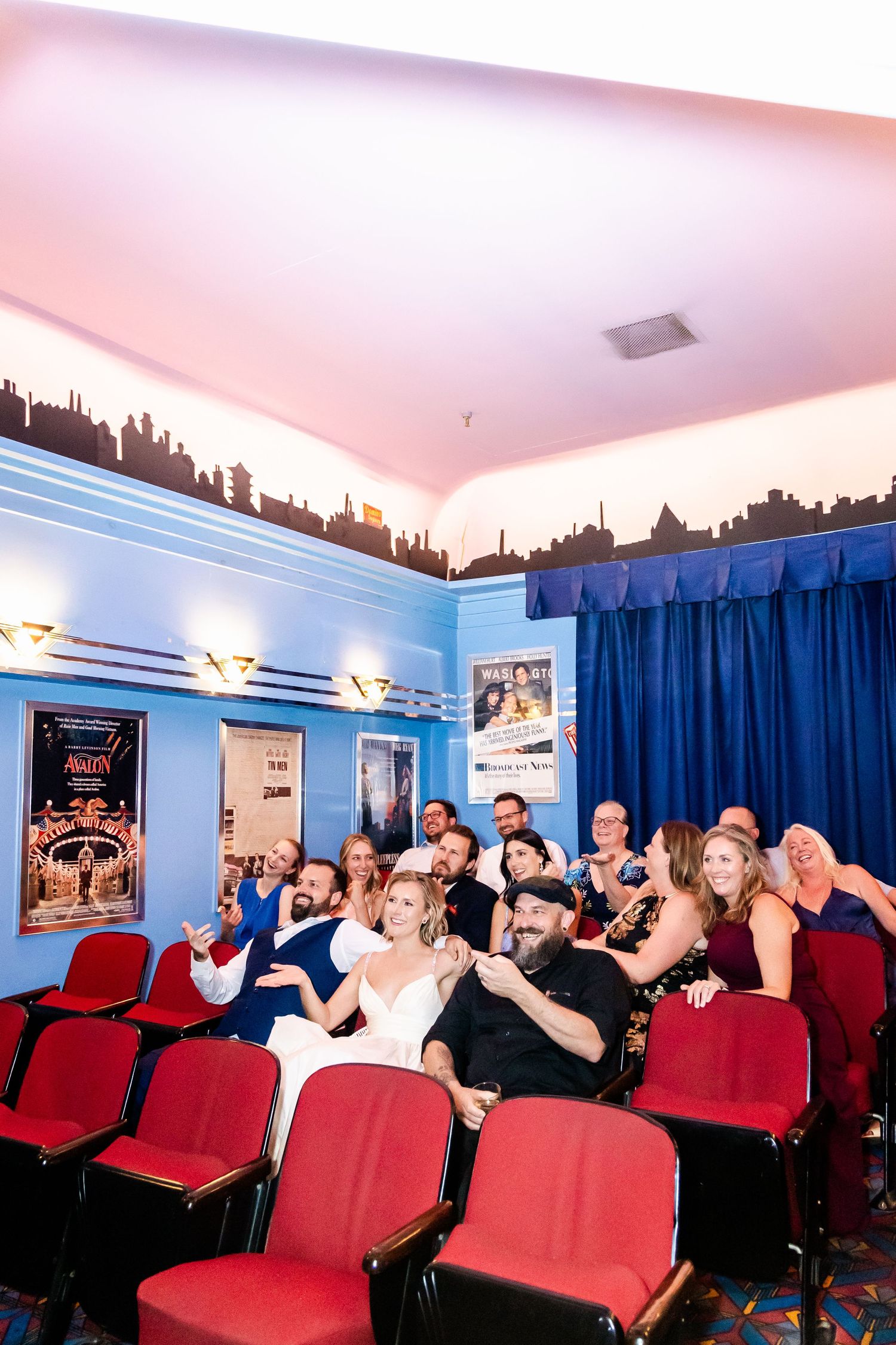 Group sitting together in theater seats with red upholstery and blue walls during a movie screening.