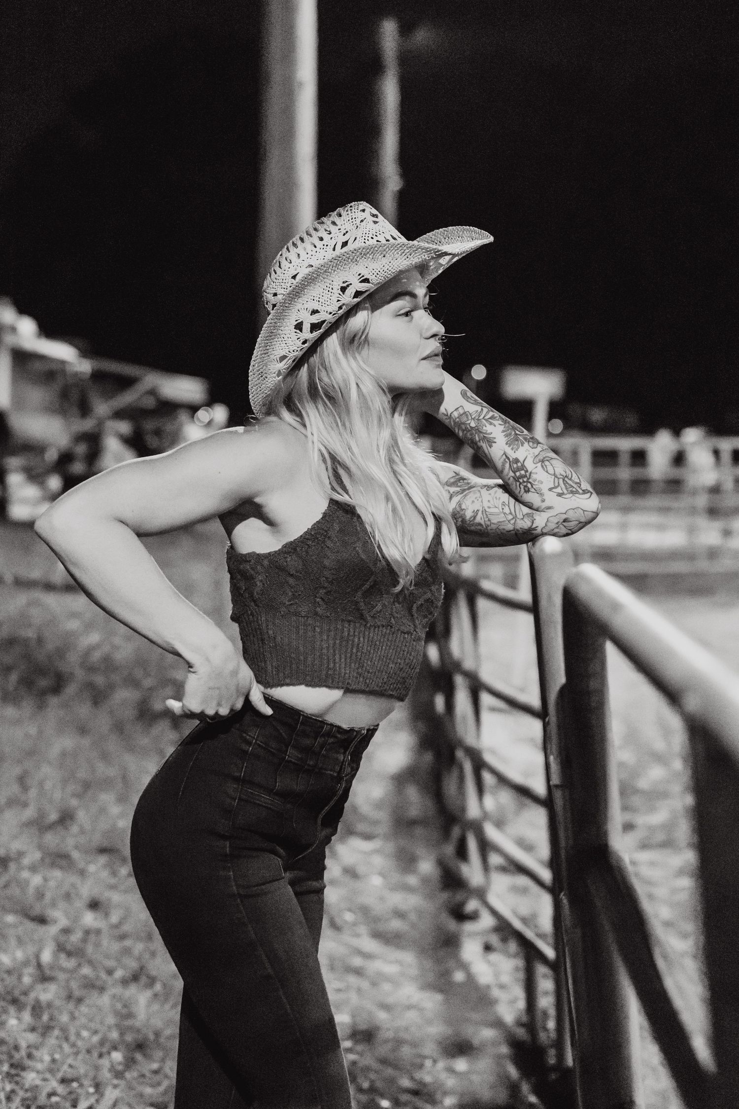 Person in a cowboy hat and country western attire leans back expressively against a wooden fence in black and white.