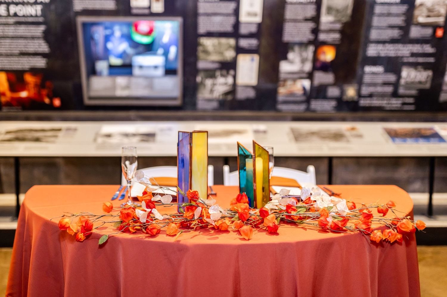 A wedding reception table decorated with fall foliage and colorful candles against a rustic backdrop.