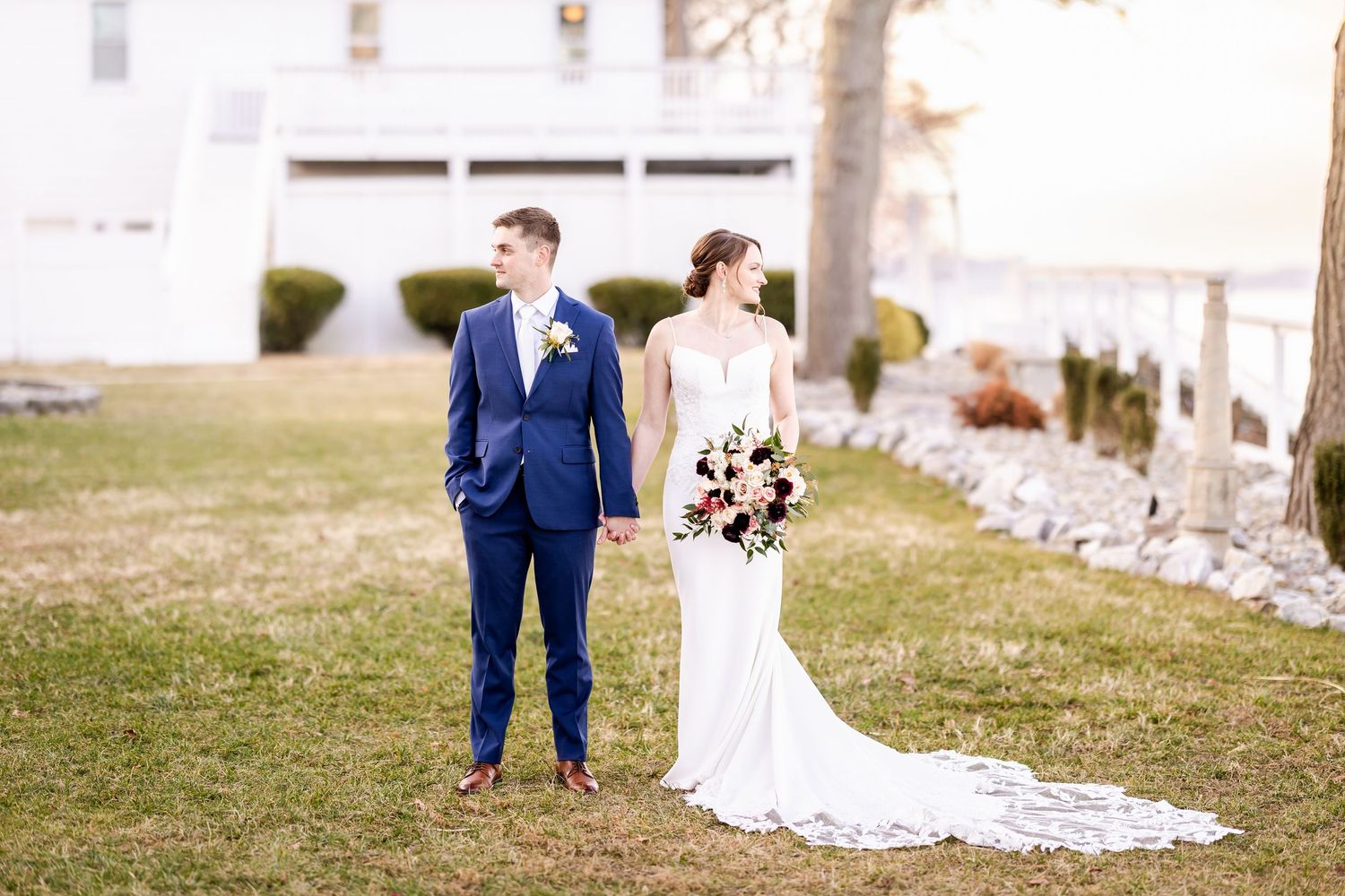 Scenic outdoor wedding ceremony with couples and guests gathered on a grassy field near elegant venue.