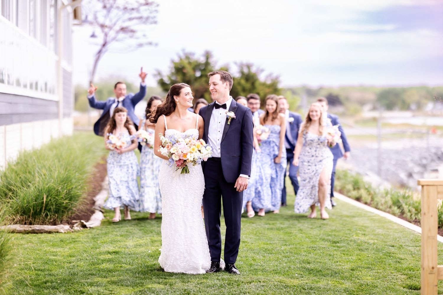 Wedding party in blue floral dresses walking along coastal path.