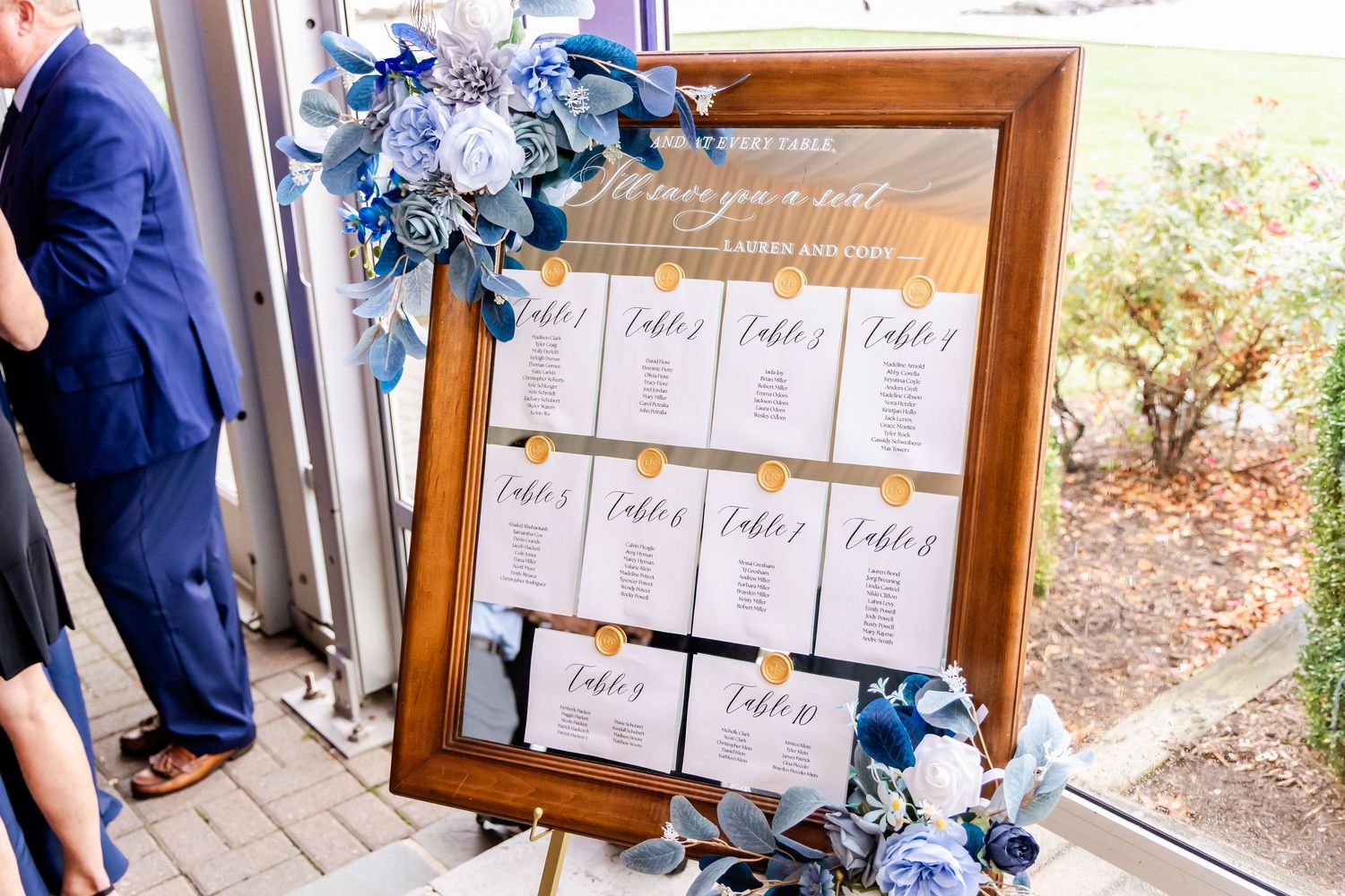 Wedding seating chart display with blue floral decorations and wooden frames.