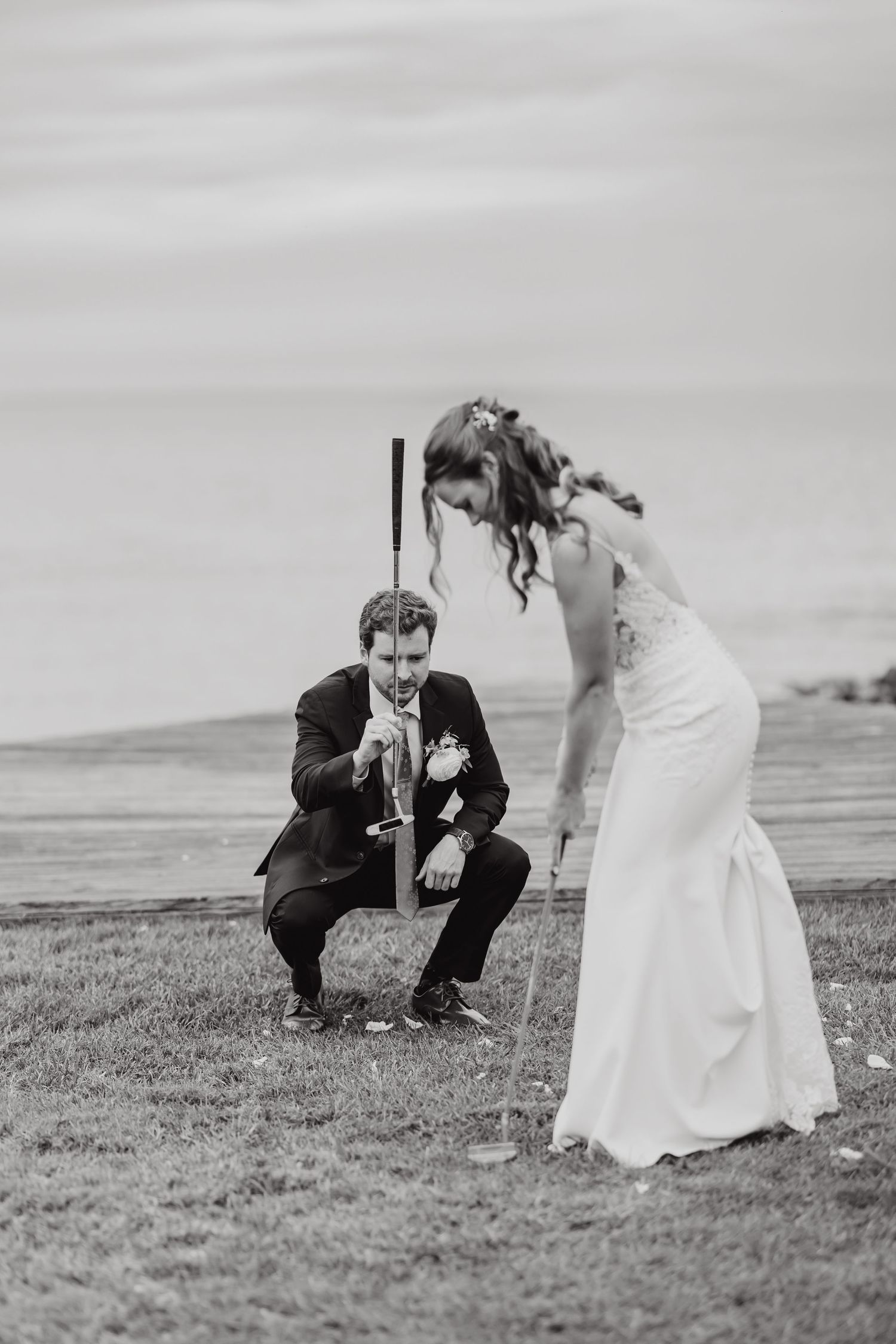 A couple in formal attire plays croquet on a grassy field in black and white.