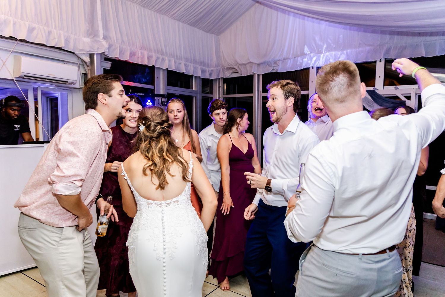 Wedding party and guests dancing energetically on a white dance floor at reception.