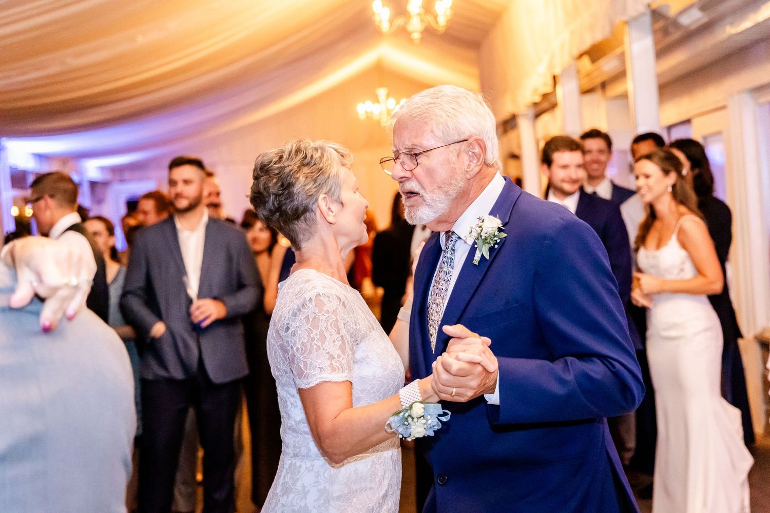 Wedding reception dance floor filled with guests enjoying themselves under warm chandelier lighting.
