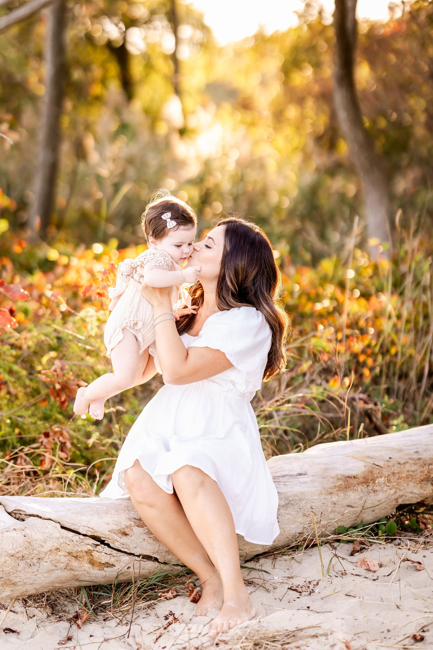 A child in a white dress lies on a fallen log at sunset in a forest setting with golden autumn light.