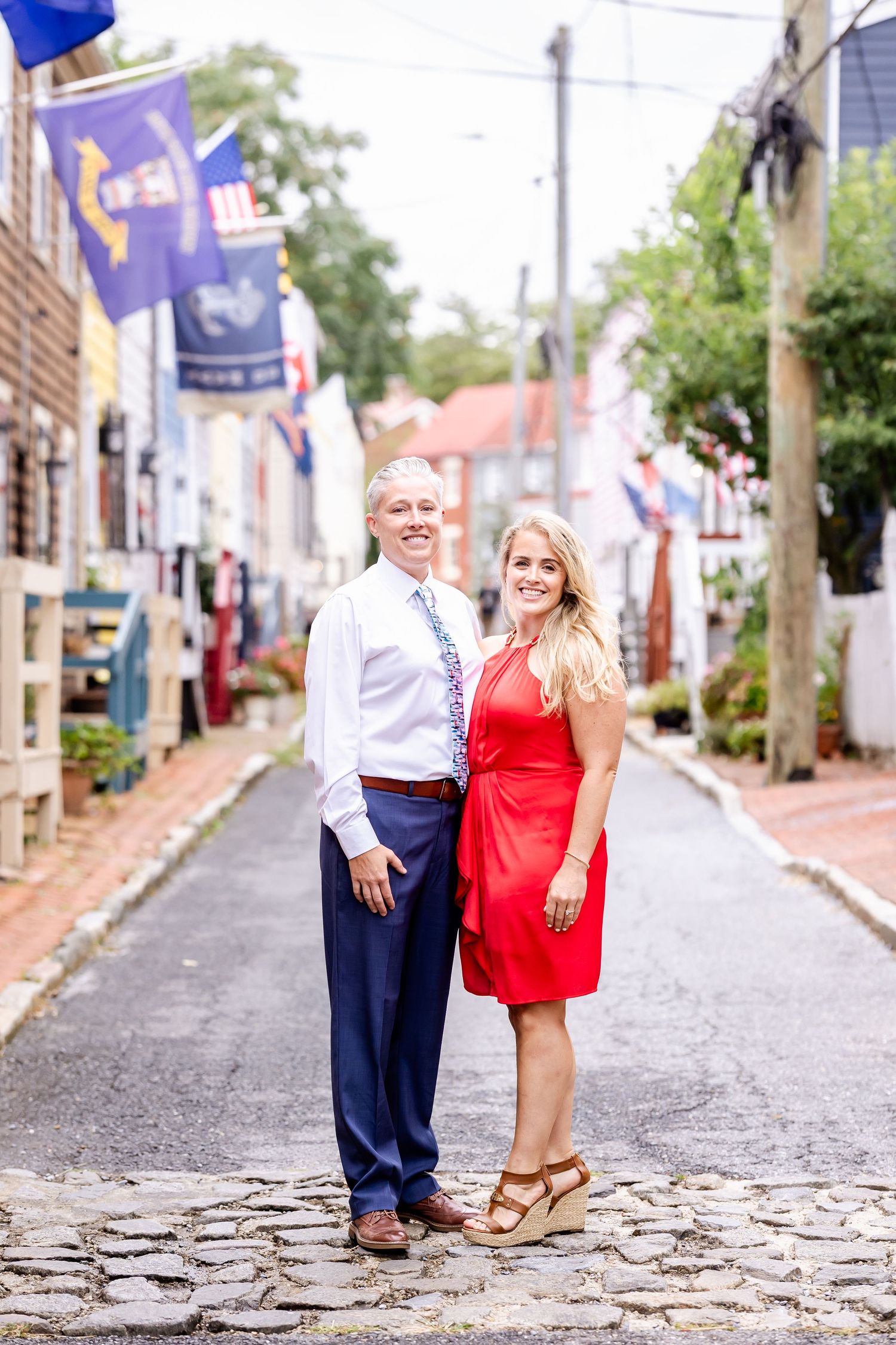 A couple poses together on a historic cobblestone street lined with flags and buildings in Annapolis, Maryland.