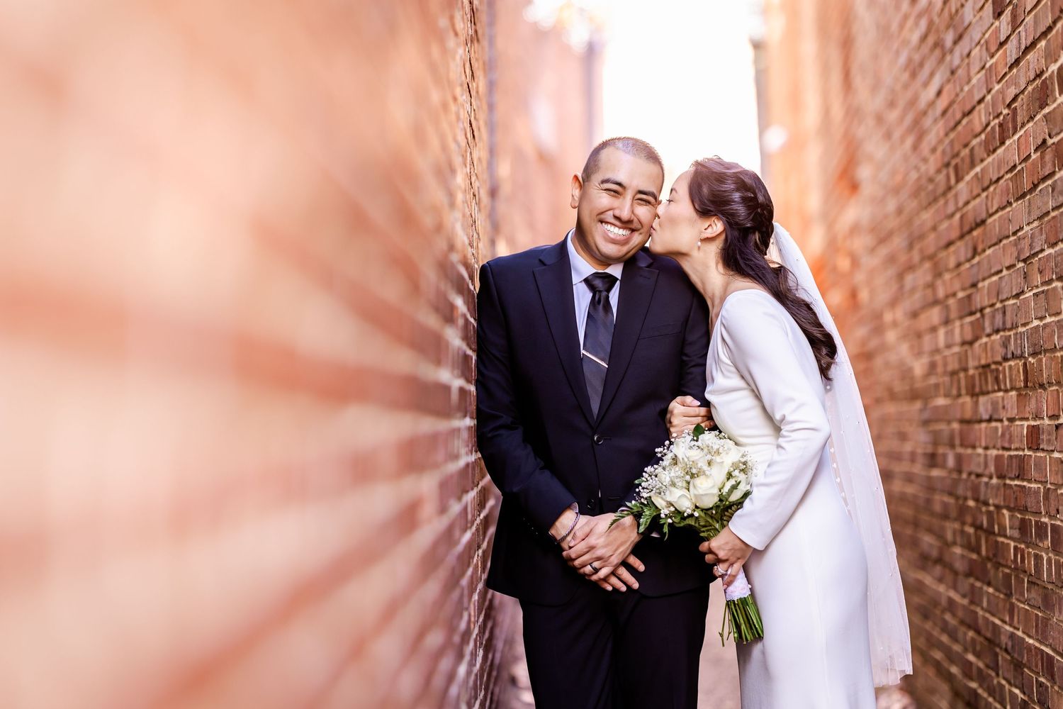 A couple shares a candid moment between brick walls on their wedding day.