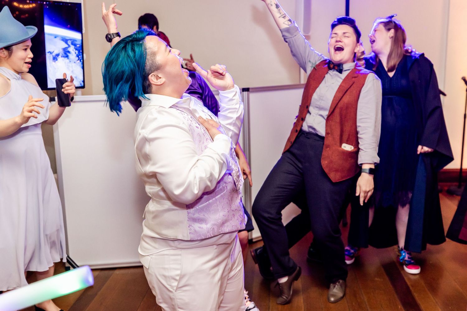 Partygoers having fun on a dance floor with blue hair and white outfit standing out in the crowd.
